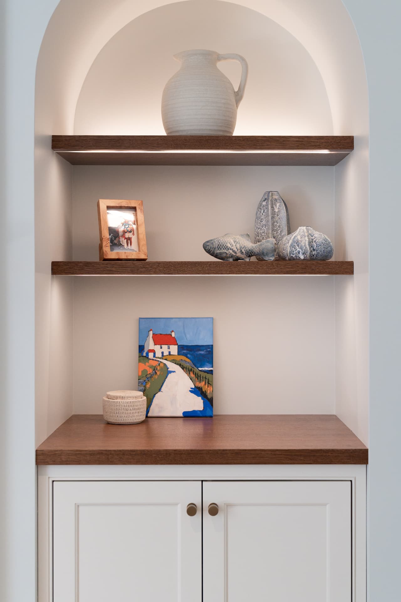Lit built-in display shelving with walnut shelves and painted lower cabinets
